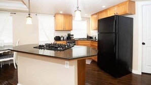 Une cuisine moderne avec des meubles en bois, un réfrigérateur noir, une cuisinière à gaz et des luminaires suspendus.
