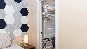Une chambre à coucher comprenant un lit, une table de chevet, une lampe, une armoire avec des vêtements suspendus et une chaise.