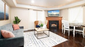 Un salon avec une cheminée, un canapé, une table à manger avec des chaises et un grand tableau accroché au mur.