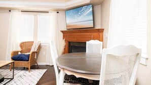 Un salon avec une cheminée, un téléviseur fixé au-dessus et deux fauteuils.