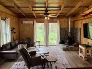 A cozy cabin interior with a leather sofa, a wooden coffee table, a stone fireplace, and a television.