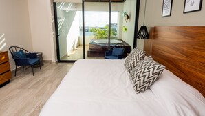 Ein modernes Hotelzimmer mit einem großen Bett, einem kleinen Schreibtisch, einem Sessel und einem Balkon mit Whirlpool.