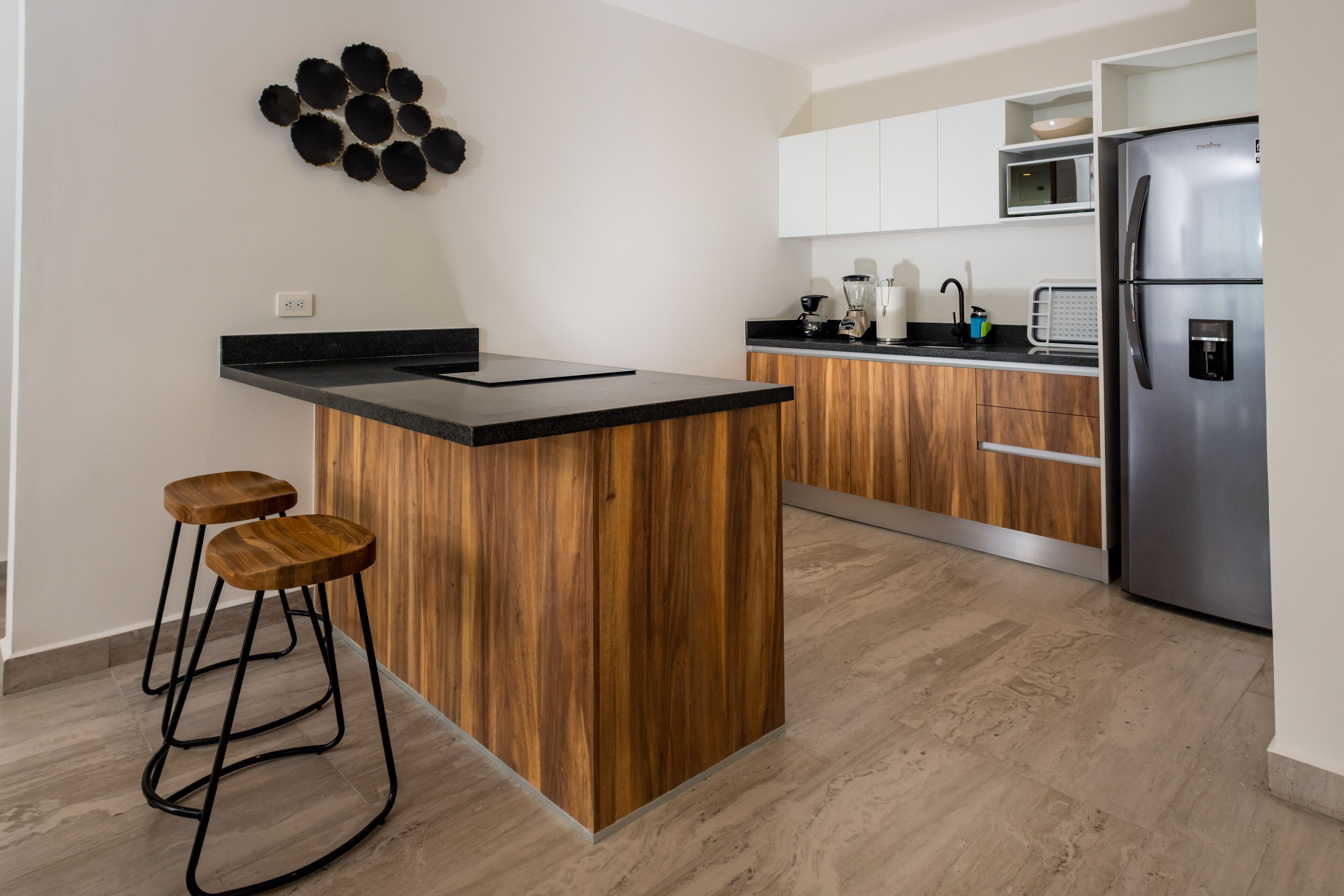 Una cucina moderna con isola centrale, sgabelli da bar in legno, frigorifero in acciaio inossidabile e pensili bianchi.