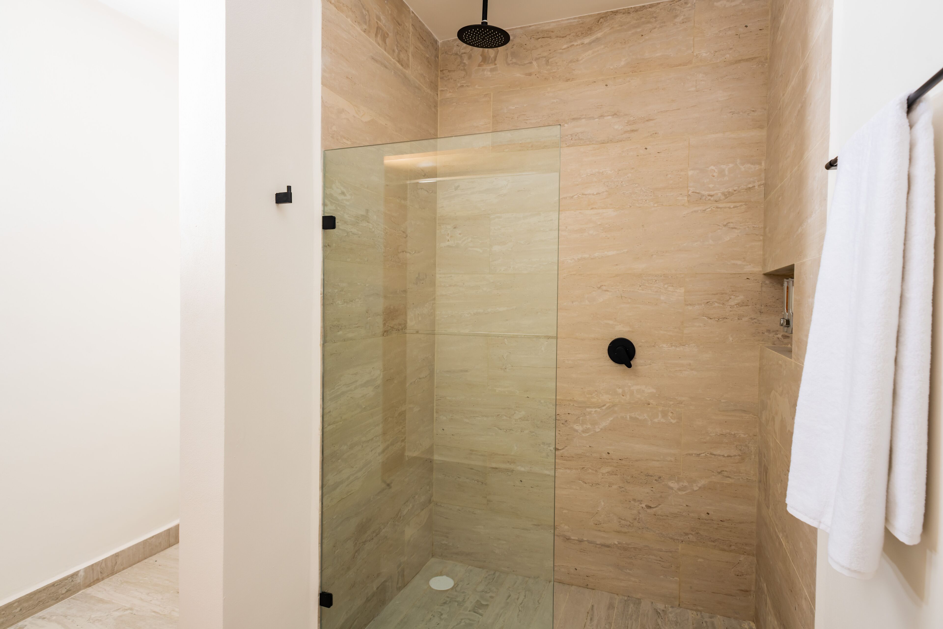 A glass-enclosed shower with beige marble walls and a white towel hanging on the wall.