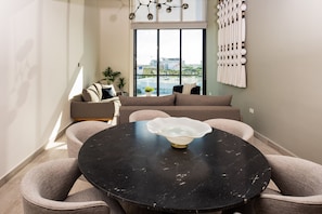 Ein modernes Wohnzimmer mit einem runden schwarzen Tisch, einem beige farbenen Sofa und einem großen Fenster mit Blick auf die Stadt.