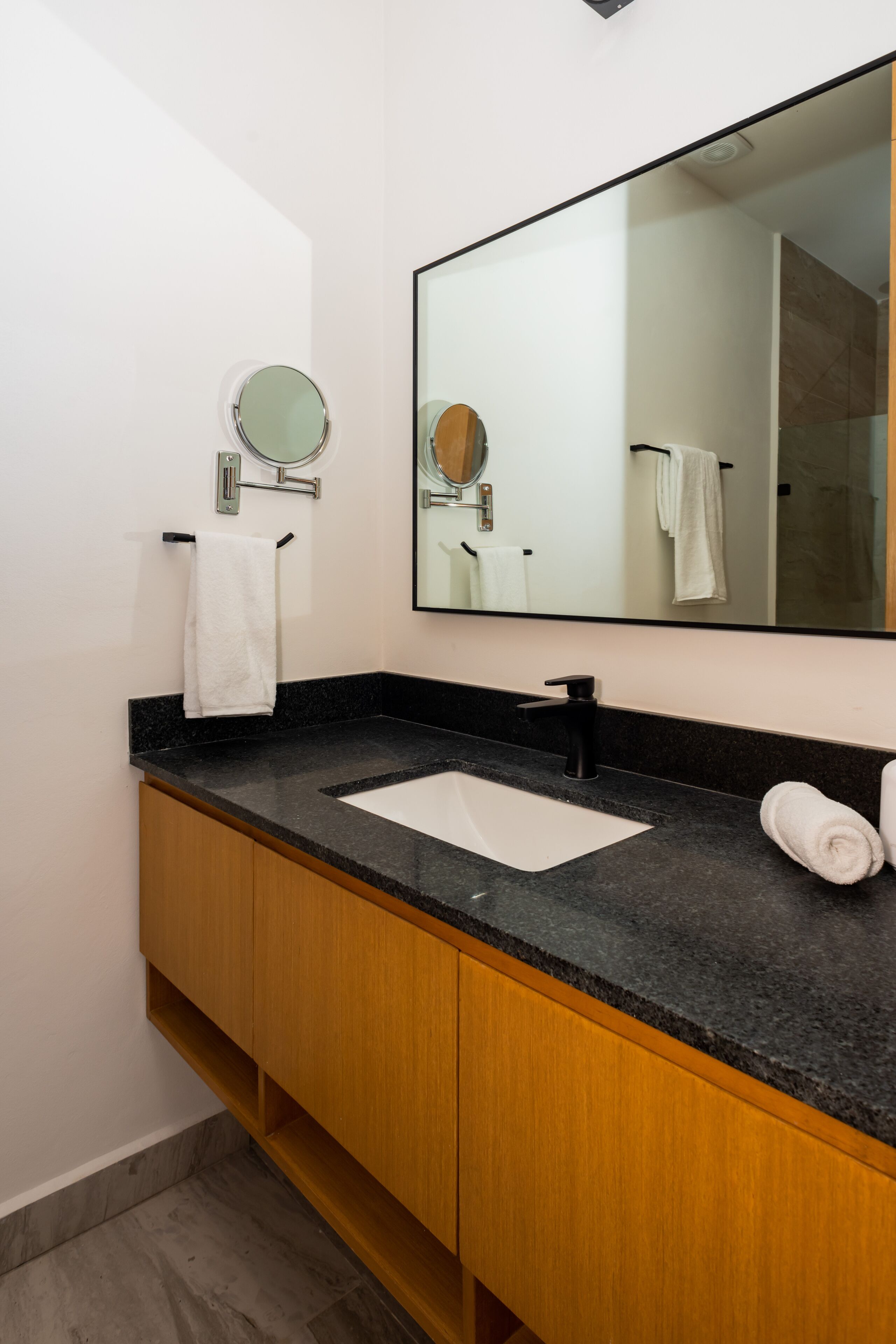 A bathroom with a black granite countertop, a white sink, wooden cabinets, a round mirror, and a white towel.
