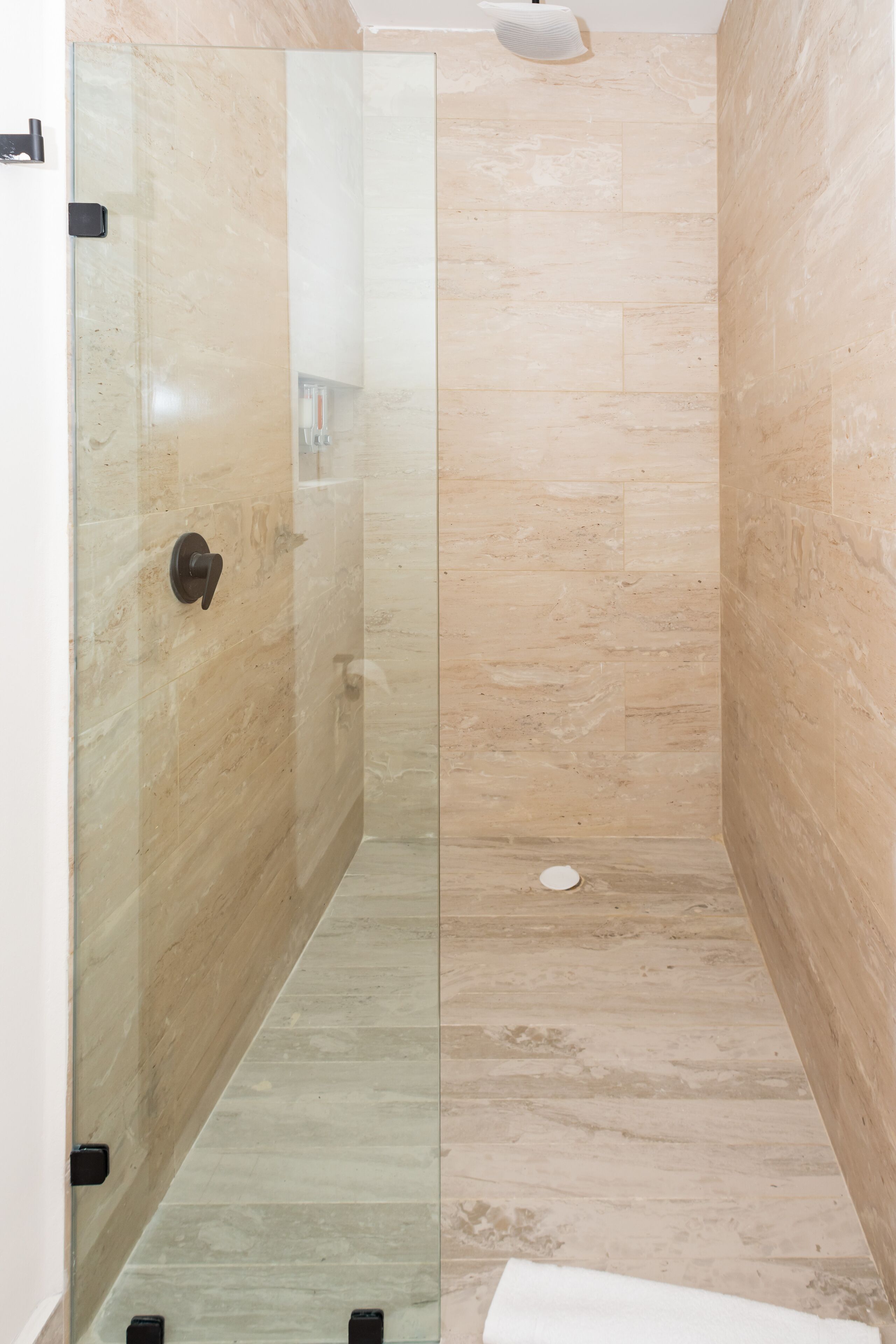 A modern bathroom with a glass shower enclosure, marble walls, and a tiled floor.