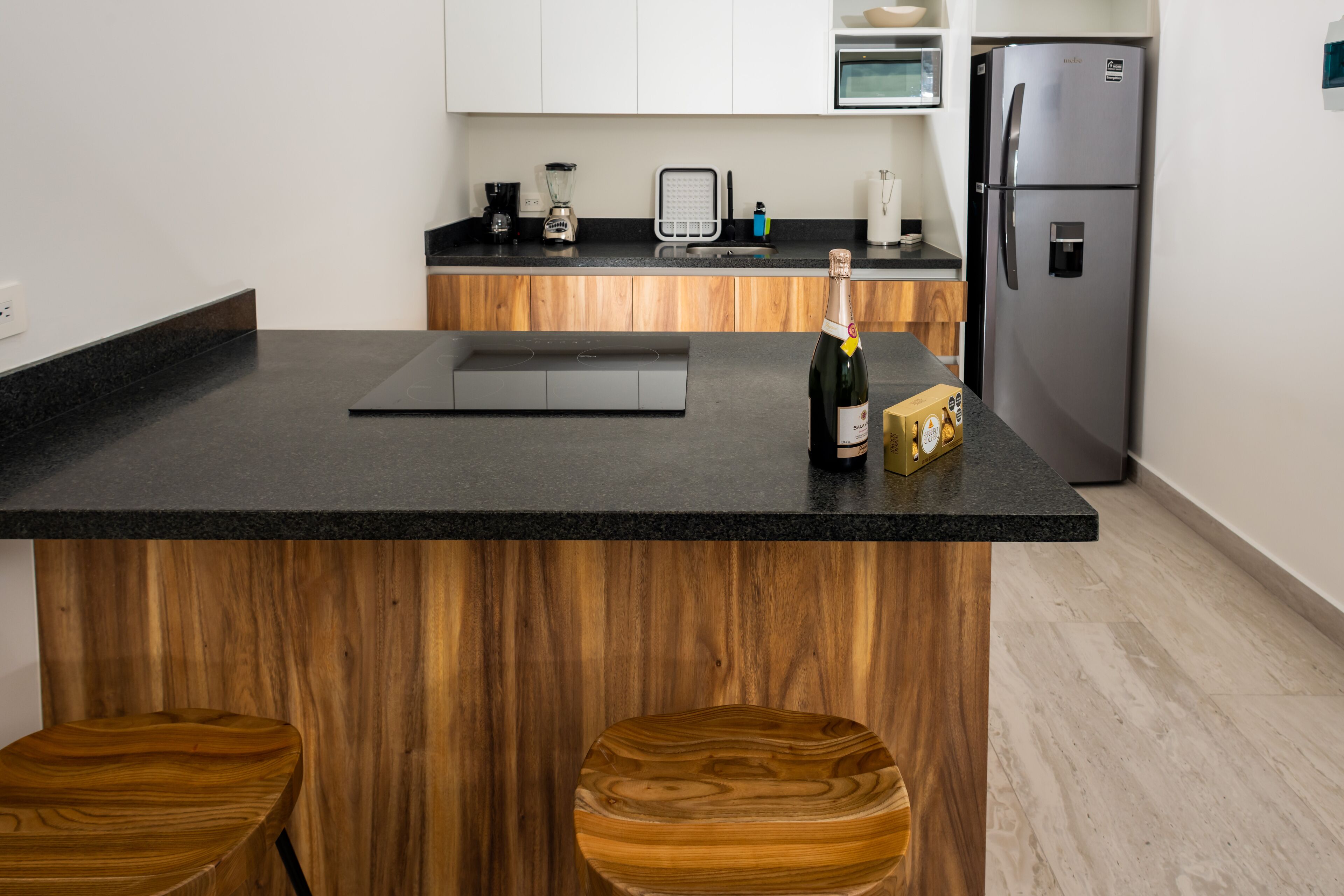 Une cuisine moderne dotée d’un îlot central, de tabourets en bois, d’un réfrigérateur et d’un four à micro-ondes.