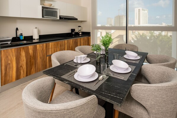 A modern dining area with a black table set for four, surrounded by beige chairs. A kitchen with white cabinets and a black countertop is visible in the background. - Torre Sofia Cancun (Cancun)