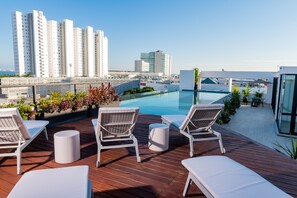 Un área de piscina en la azotea con sillones de descanso, una piscina pequeña y vistas a edificios altos.