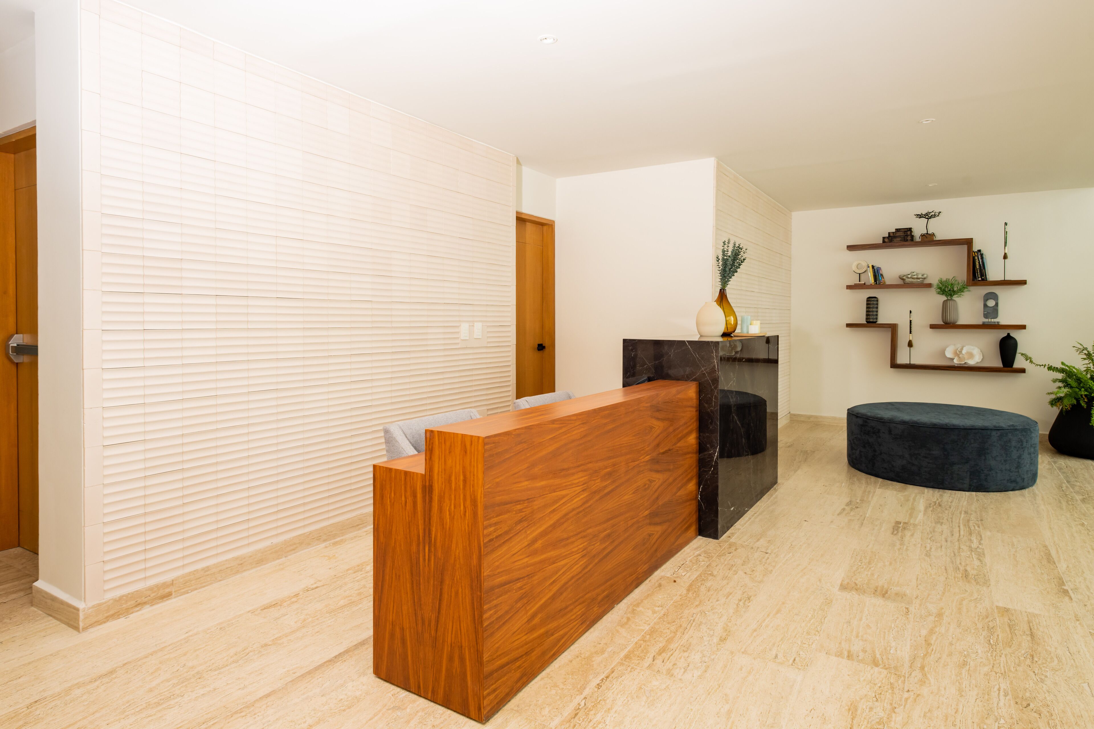 A reception area with a wooden reception desk, a dark marble fireplace, and a blue ottoman.