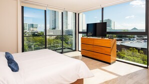 Ein modernes Schlafzimmer mit einem großen Bett, einer hölzernen Kommode und einem Fernseher. Es verfügt über große Fenster mit Blick auf die Stadt.
