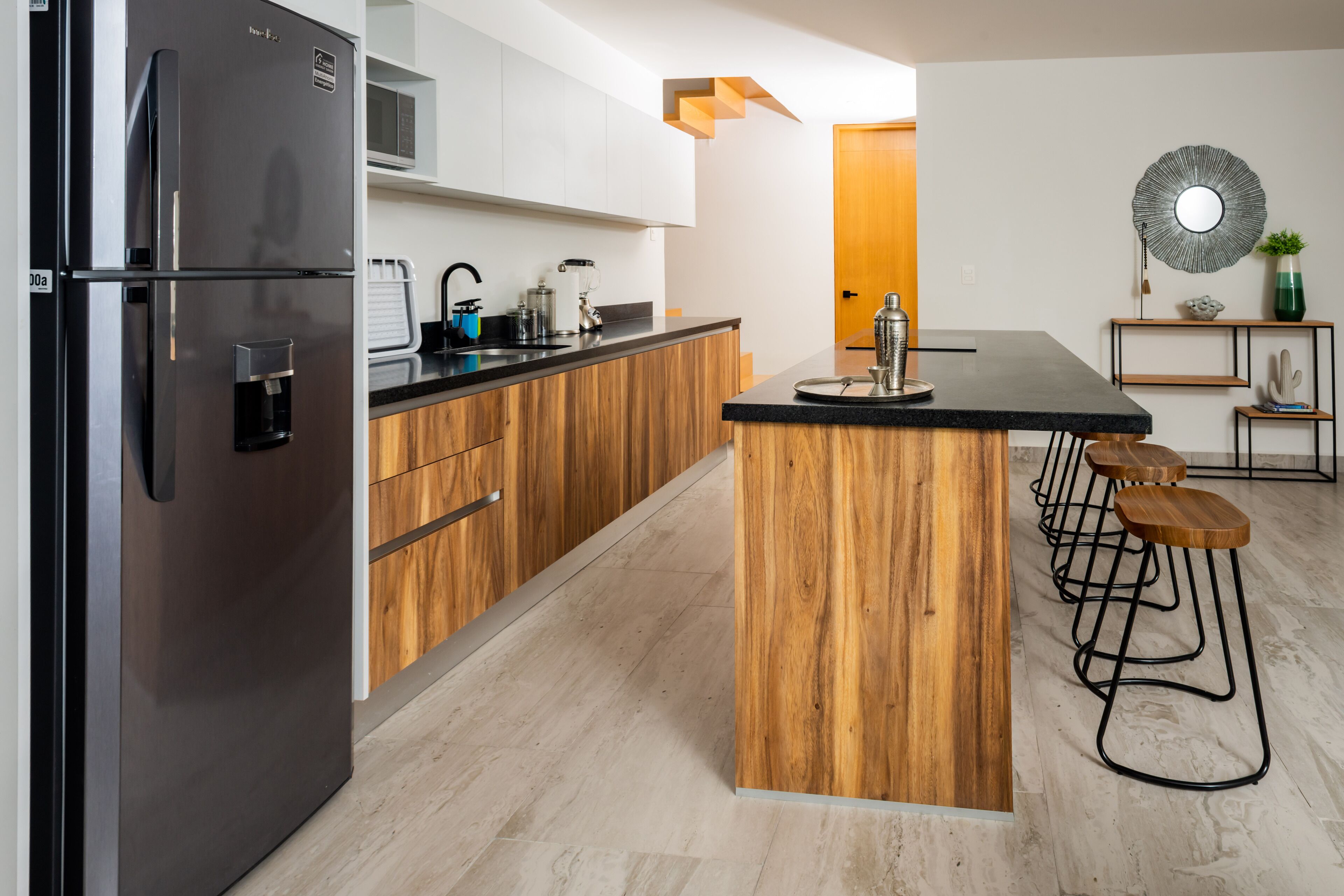 Eine moderne Küche mit einem eingebauten Kühlschrank, Holzschränken, einer schwarzen Arbeitsplatte und Barhocker.