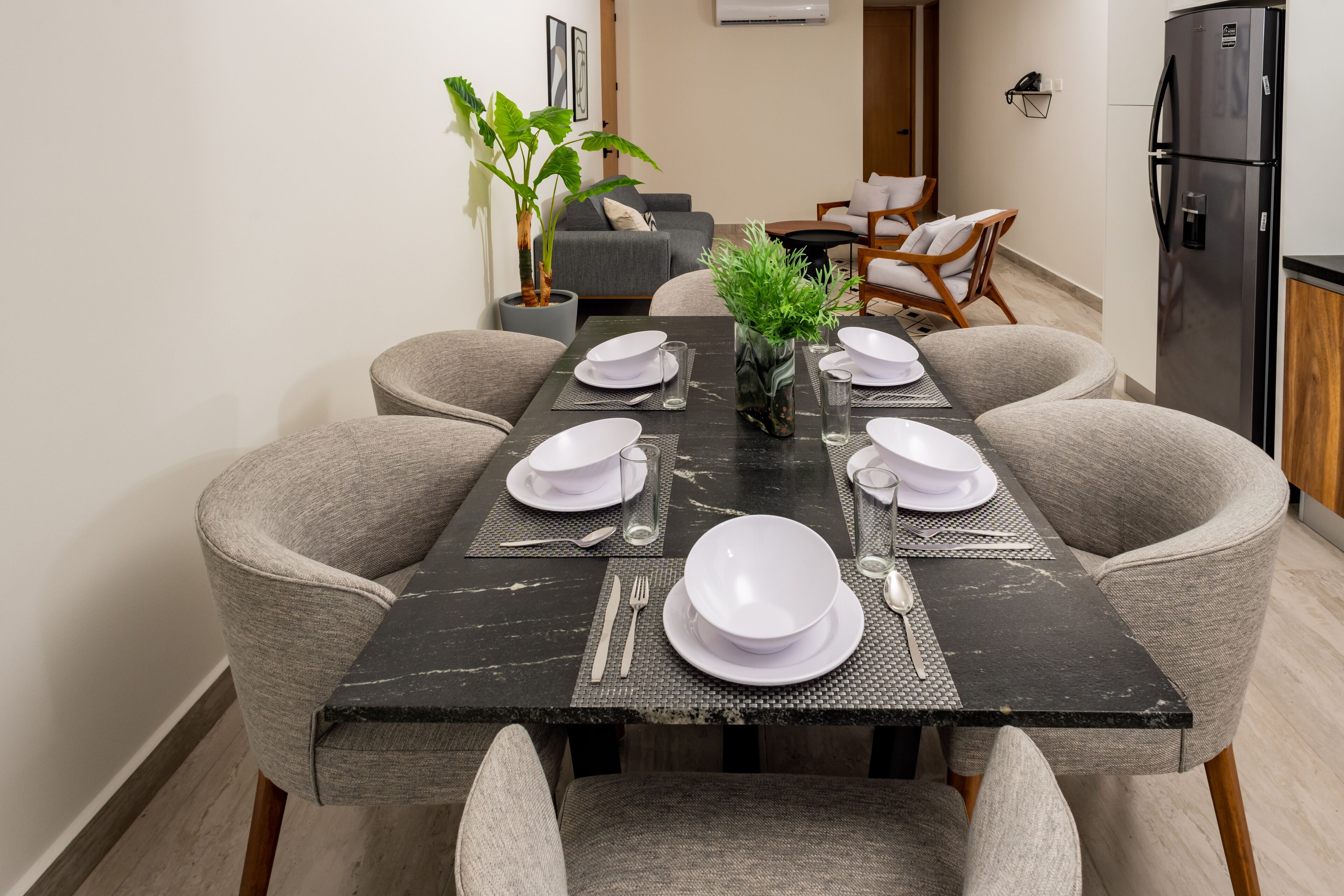 A dining area with a black marble table set for six, surrounded by grey upholstered chairs.