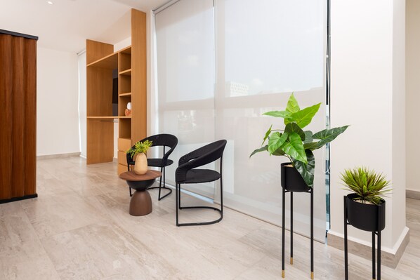A modern interior with a wooden cabinet, two black chairs, a small table with a vase and plant, and potted plants on stands. - Torre Sofia Cancun (Cancun)