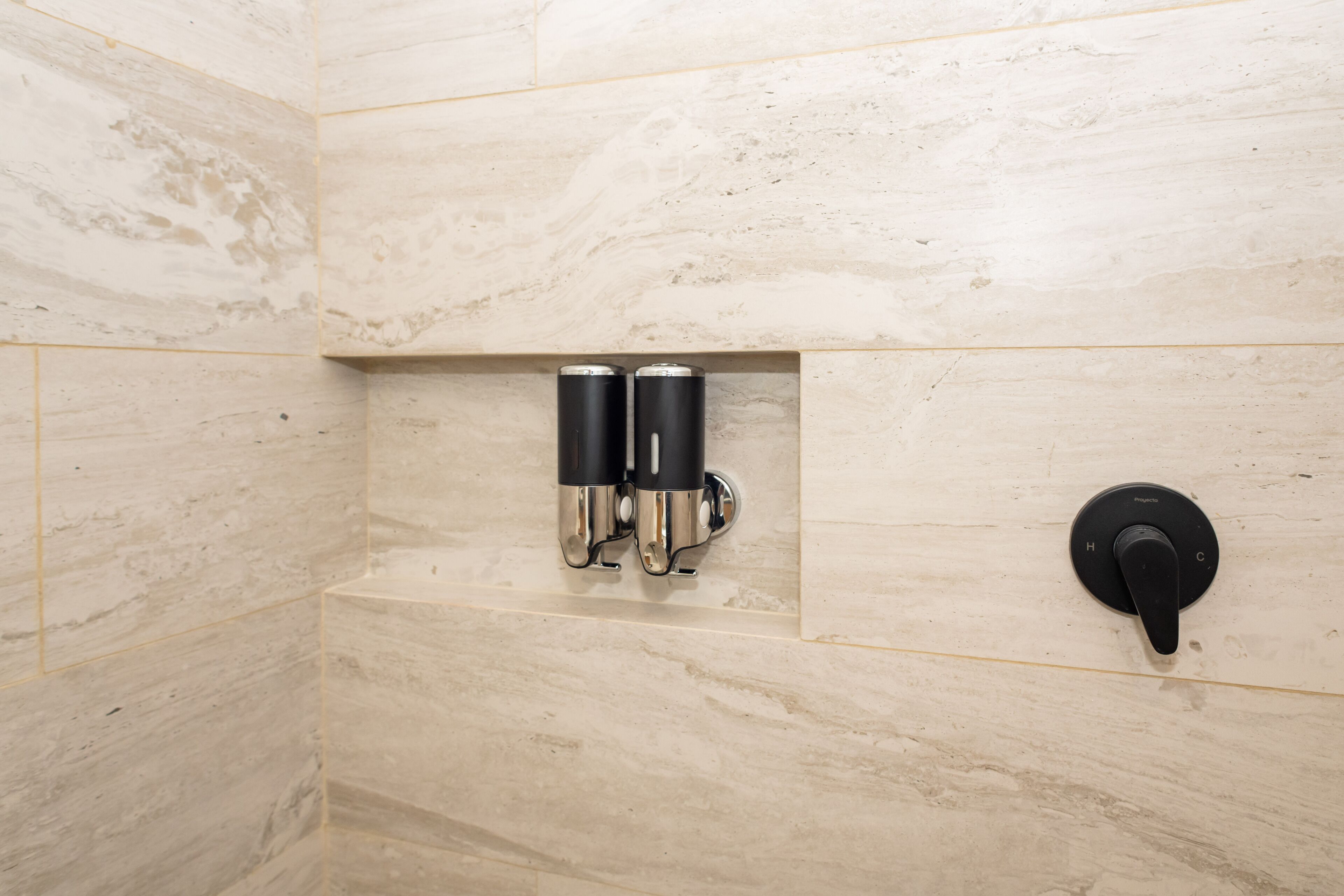 Un baño con pared de mármol, un grifo negro y dos dispensadores de jabón negros.