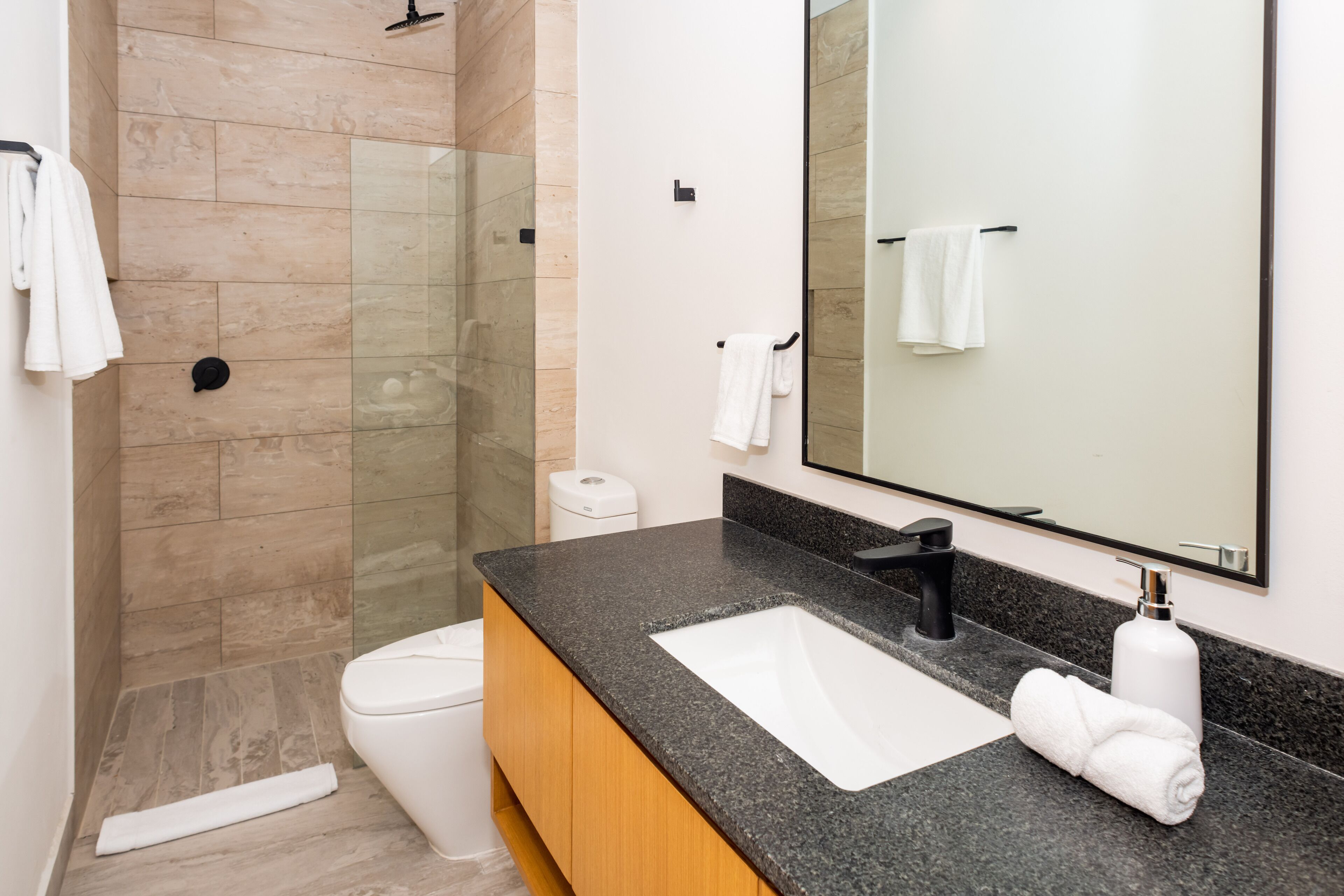 A modern bathroom with a glass-enclosed shower, a white toilet, a black sink with a large mirror, and wooden cabinets.