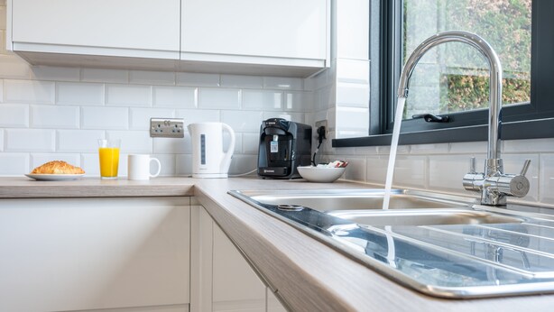 A modern kitchen with white cabinets, a stainless steel sink, and a coffee maker.