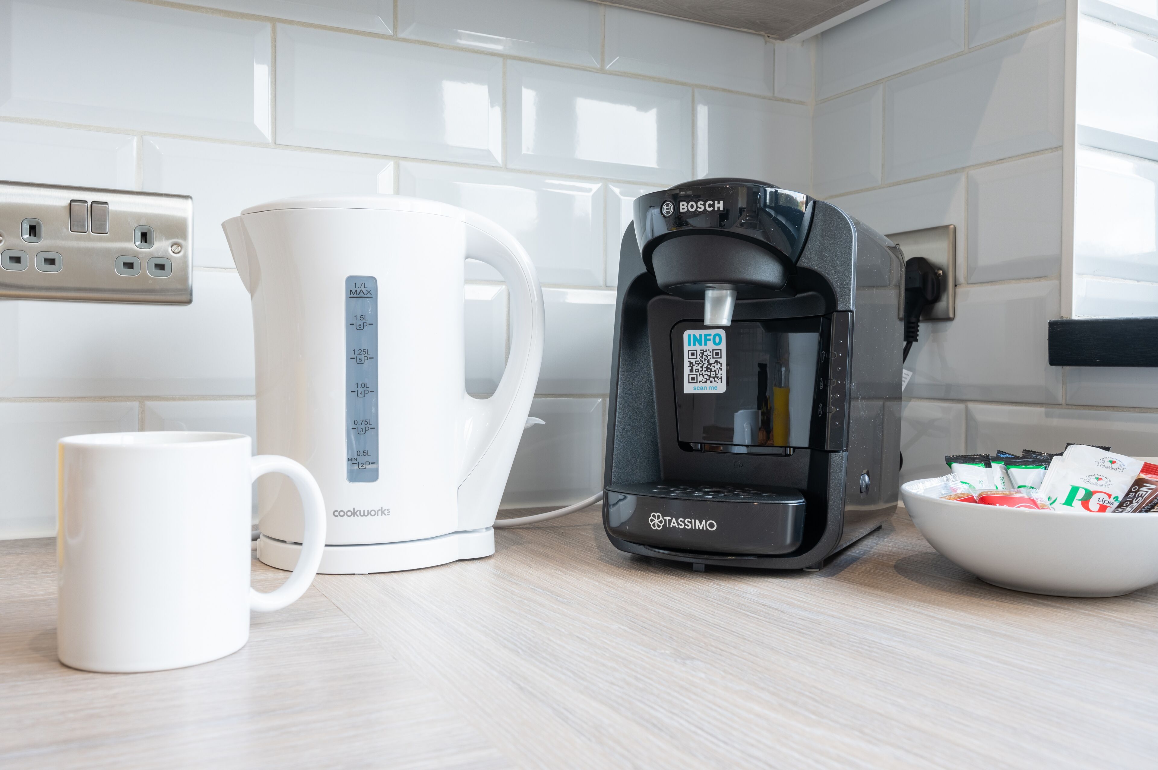 A kitchen with a coffee maker, a kettle, and a mug on the counter.