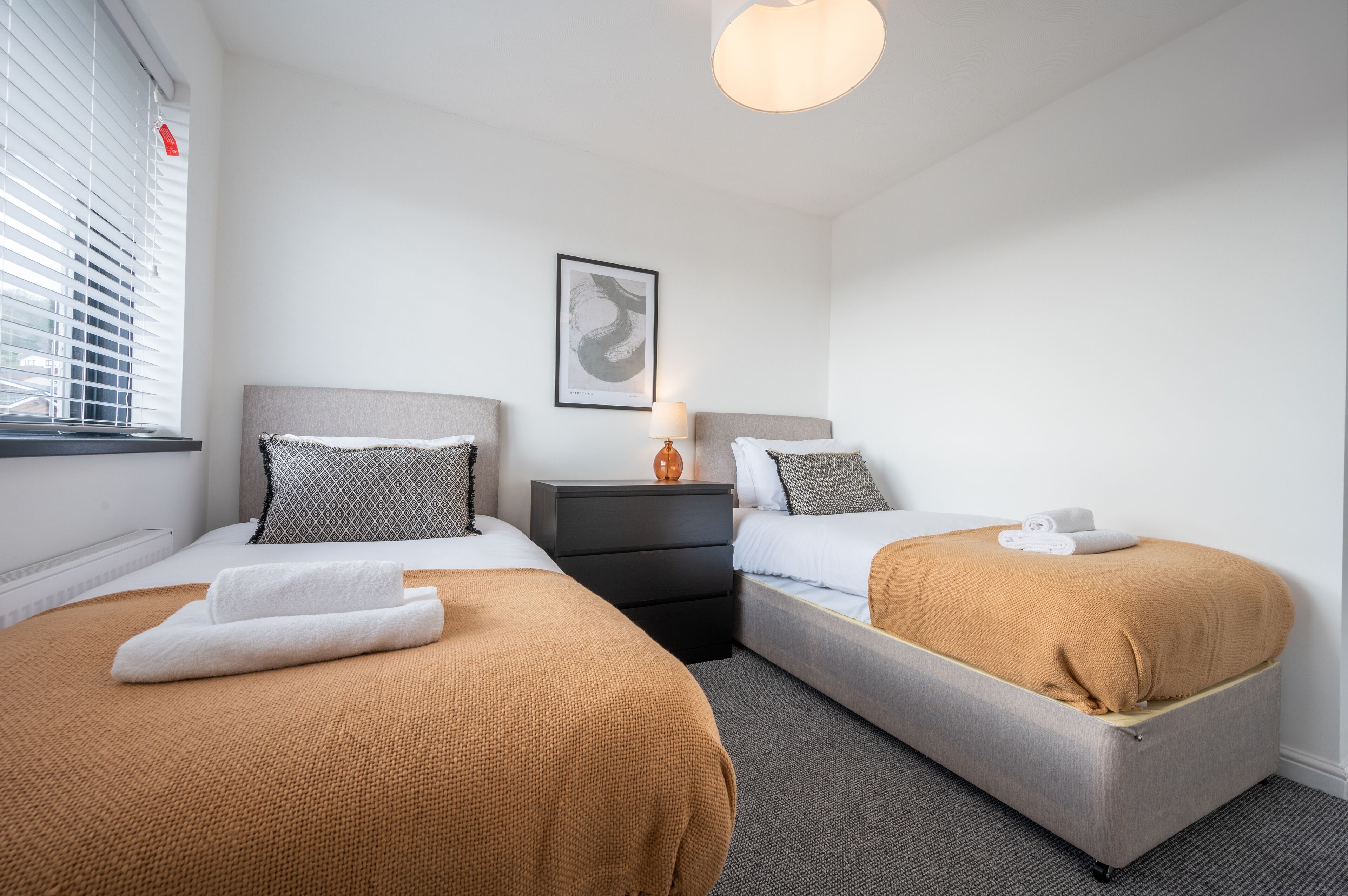 A hotel room with two beds, a nightstand, a lamp, and a framed artwork on the wall.