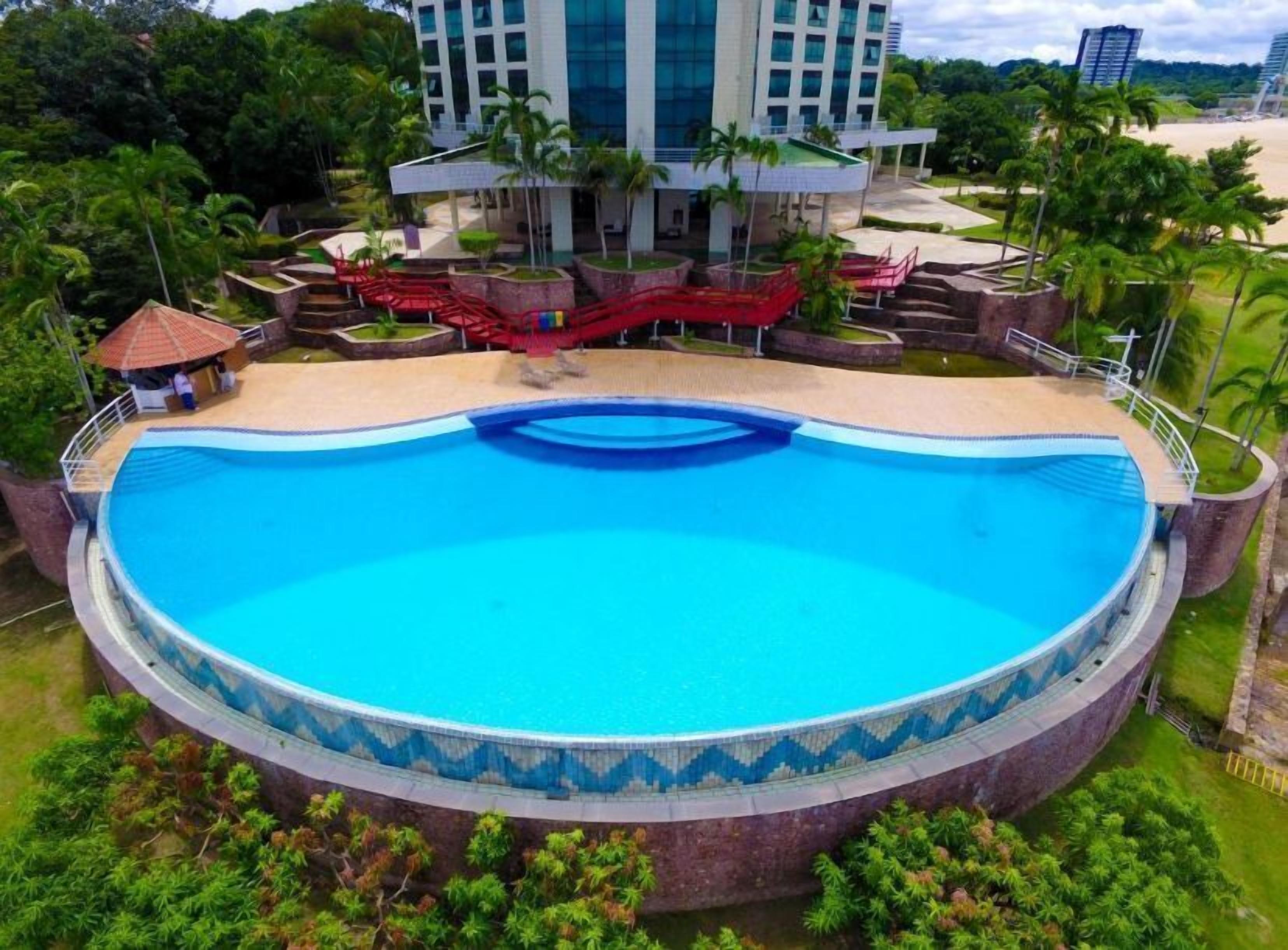 A large circular pool with a blue mosaic border, surrounded by palm trees and a modern building in the background.