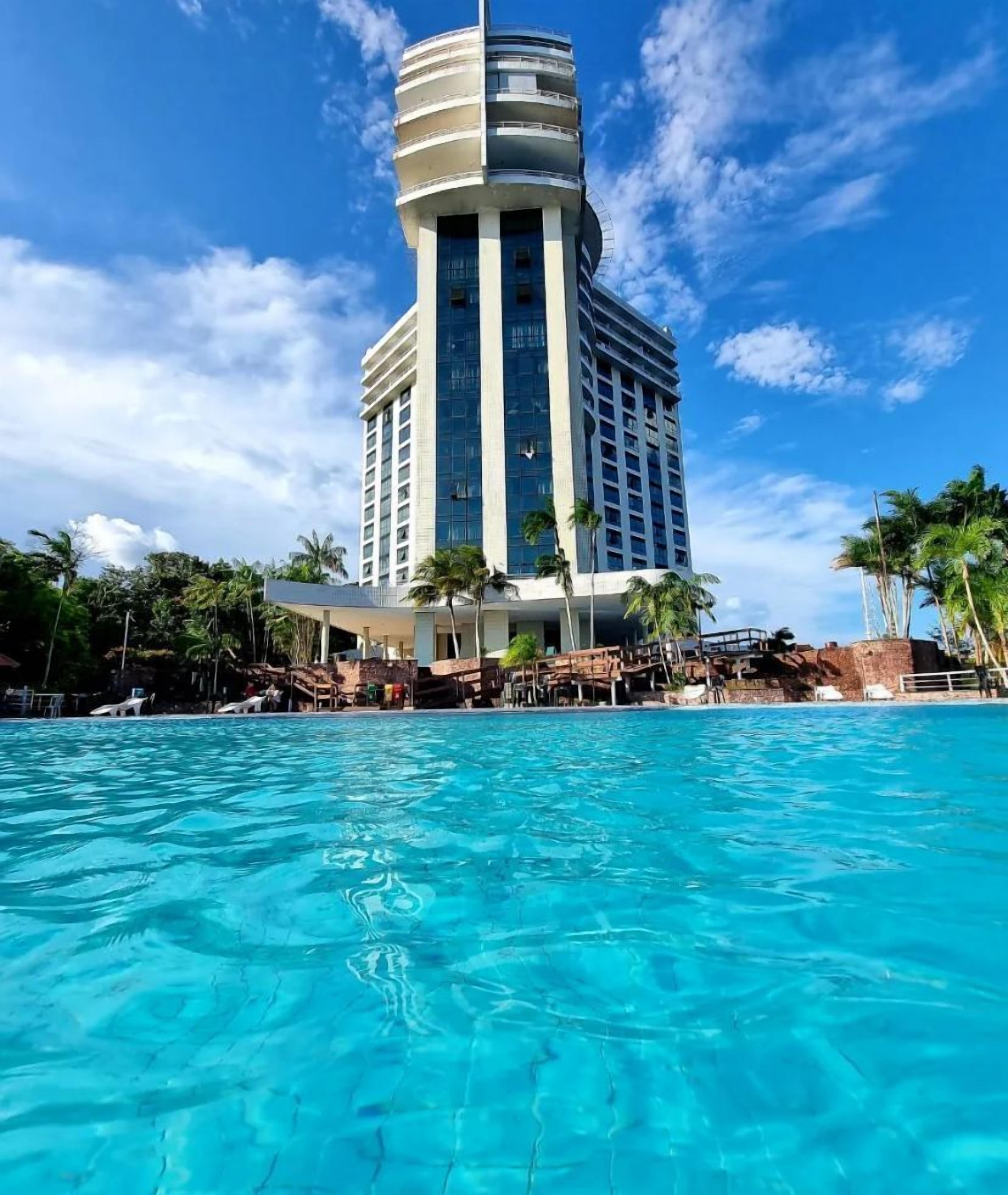 A hotel with a large pool, palm trees, and a modern building with a curved facade.