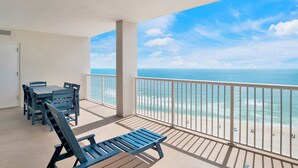 A balcony with a view of the ocean, a table with chairs, and a bench. - Summer House 1402B | Direct beach front! Oversized deck! Great location! (Orange Beach)