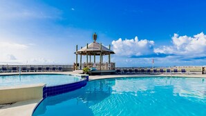 A clear blue pool with a gazebo and lounge chairs, surrounded by a wooden deck and a clear sky. - Summer House 1402B | Direct beach front! Oversized deck! Great location! (Orange Beach)