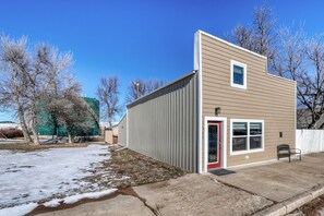 A small, single-story building with a red door and windows, adjacent to a concrete sidewalk and a snow-covered ground. - A Private, Stunning Home Walking Distance to Food, Drinks, & Parks (Whitewood)