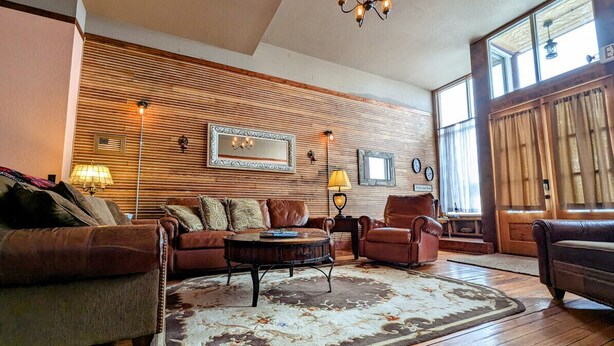 A cozy living room with a wooden wall, a large mirror, and a chandelier. - Truly the GOAT! Hot tub, Pet friendly, Walk to bar/restaurant, Quiet, Unique (Whitewood)