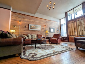 A cozy living room with a wooden wall, a large mirror, and a chandelier. - Truly the GOAT! Hot tub, Pet friendly, Walk to bar/restaurant, Quiet, Unique (Whitewood)