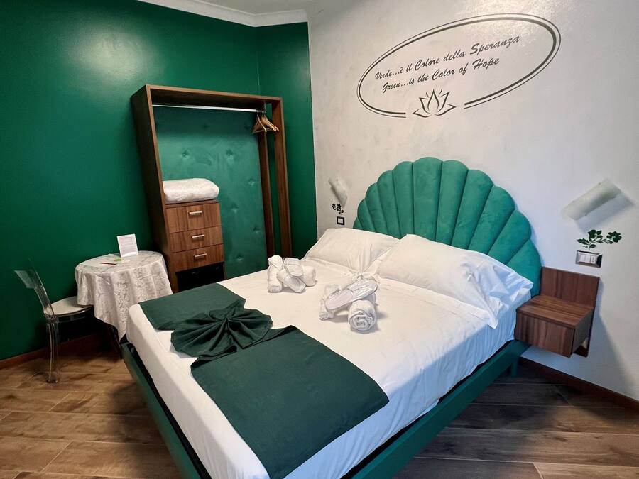 A neatly made bed with a green headboard, a small bedside table, and a wall decoration.