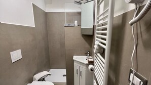 Un baño moderno con inodoro, bidé, lavamanos y ducha a ras de suelo.