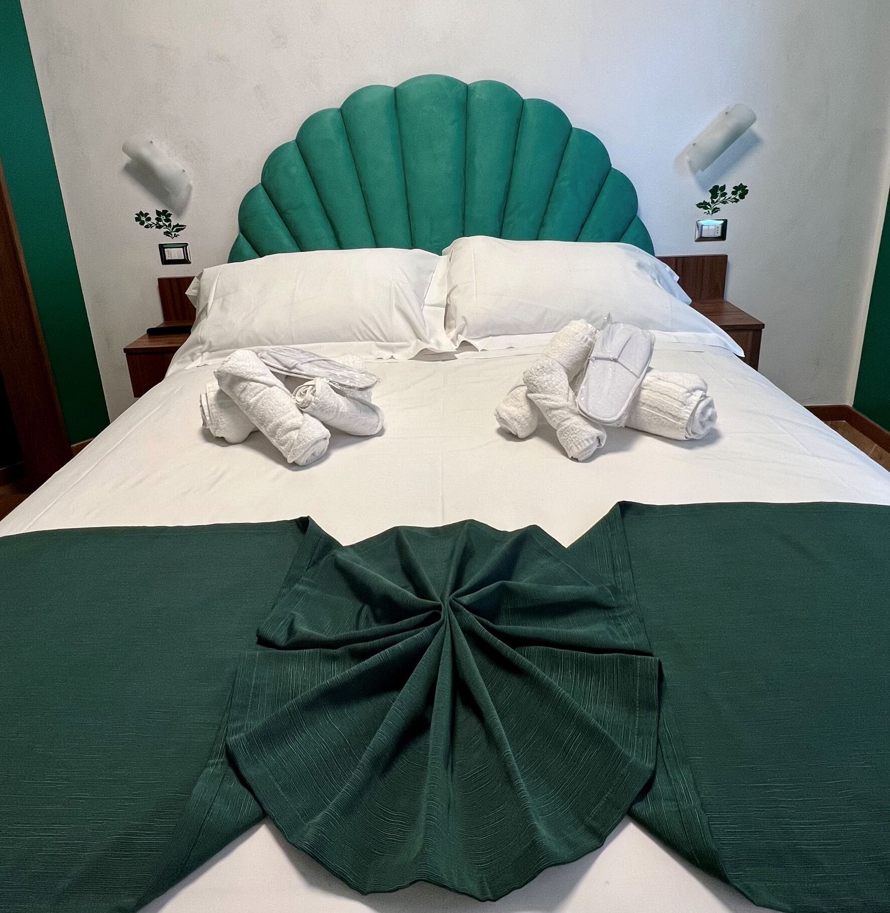 Een net opgemaakt bed met witte lakens, een groen gestoffeerd hoofdeinde en een decoratief groen stoffen einde.