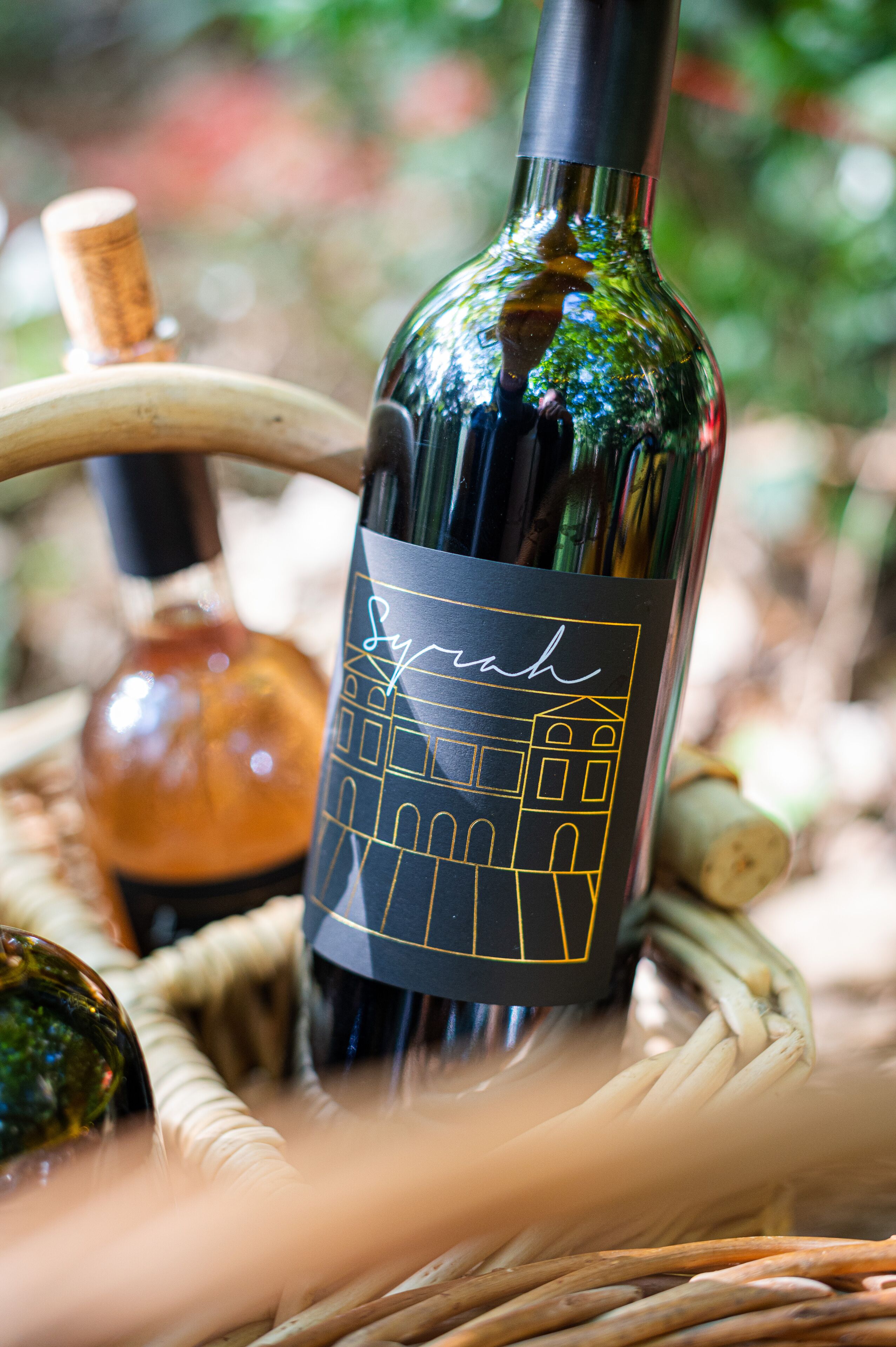 A wine bottle with a black label and gold outline, placed in a wicker basket.
