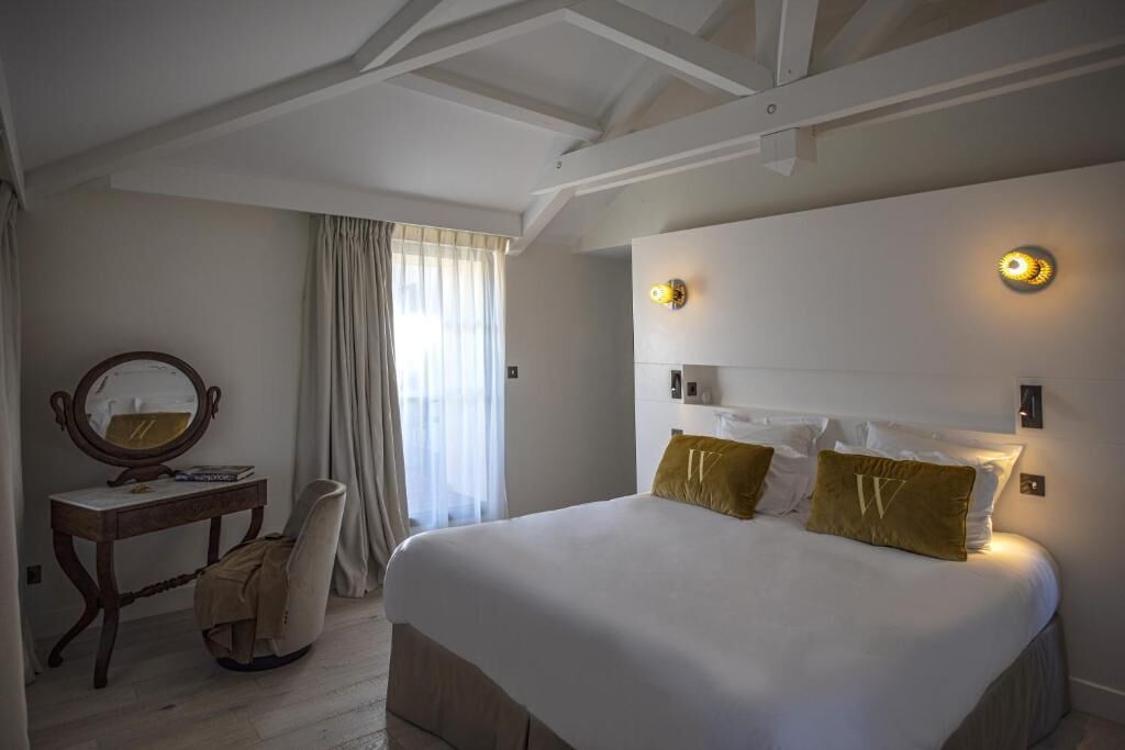Habitación de hotel con una cama grande, un escritorio con silla, un espejo y dos lámparas de pared.