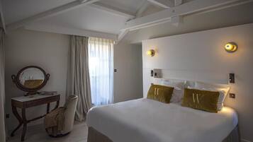 Habitación de hotel con una cama grande, un escritorio con silla, un espejo y dos lámparas de pared.
