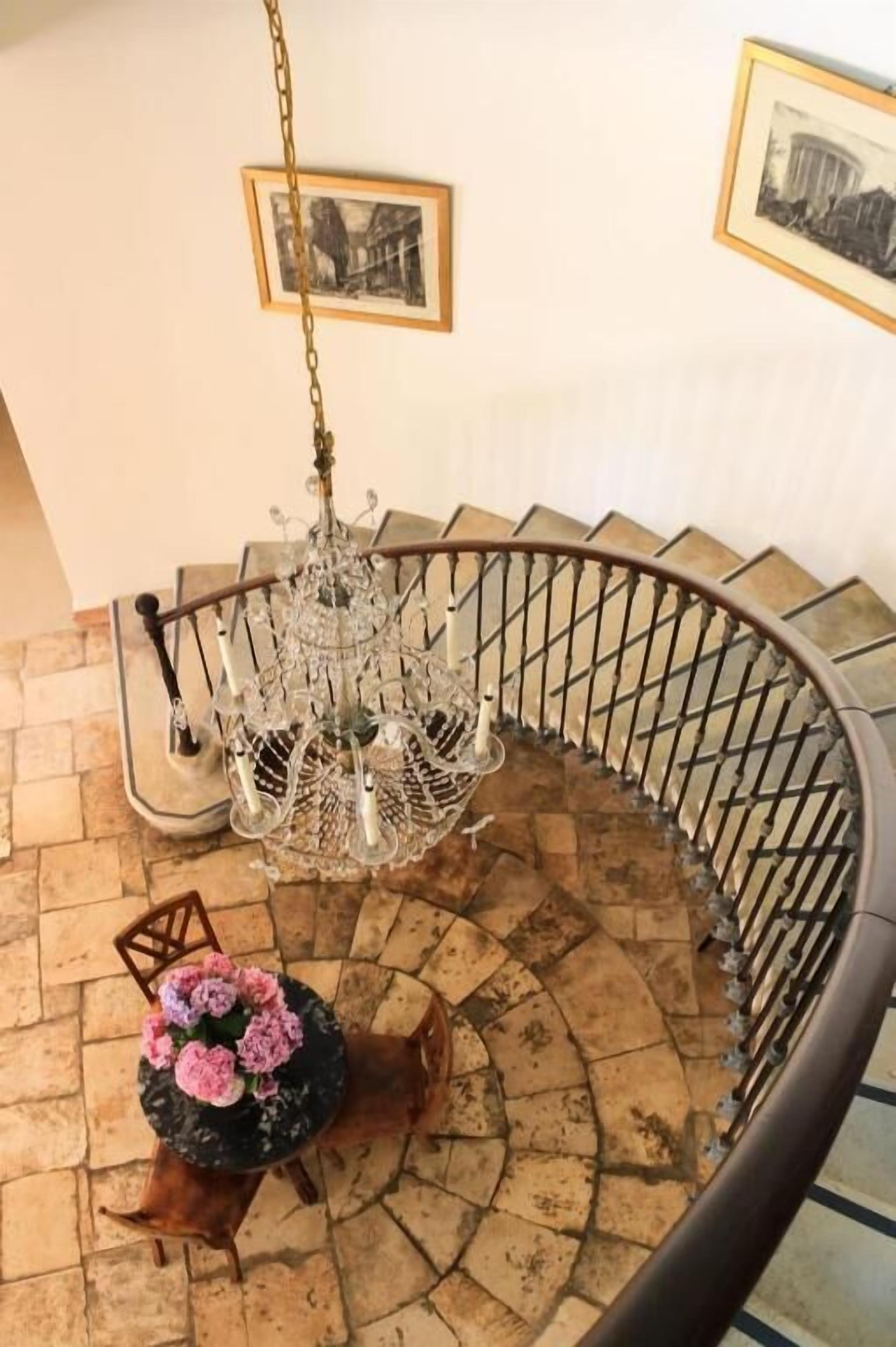 A spiral staircase with a chandelier and framed pictures on the walls.