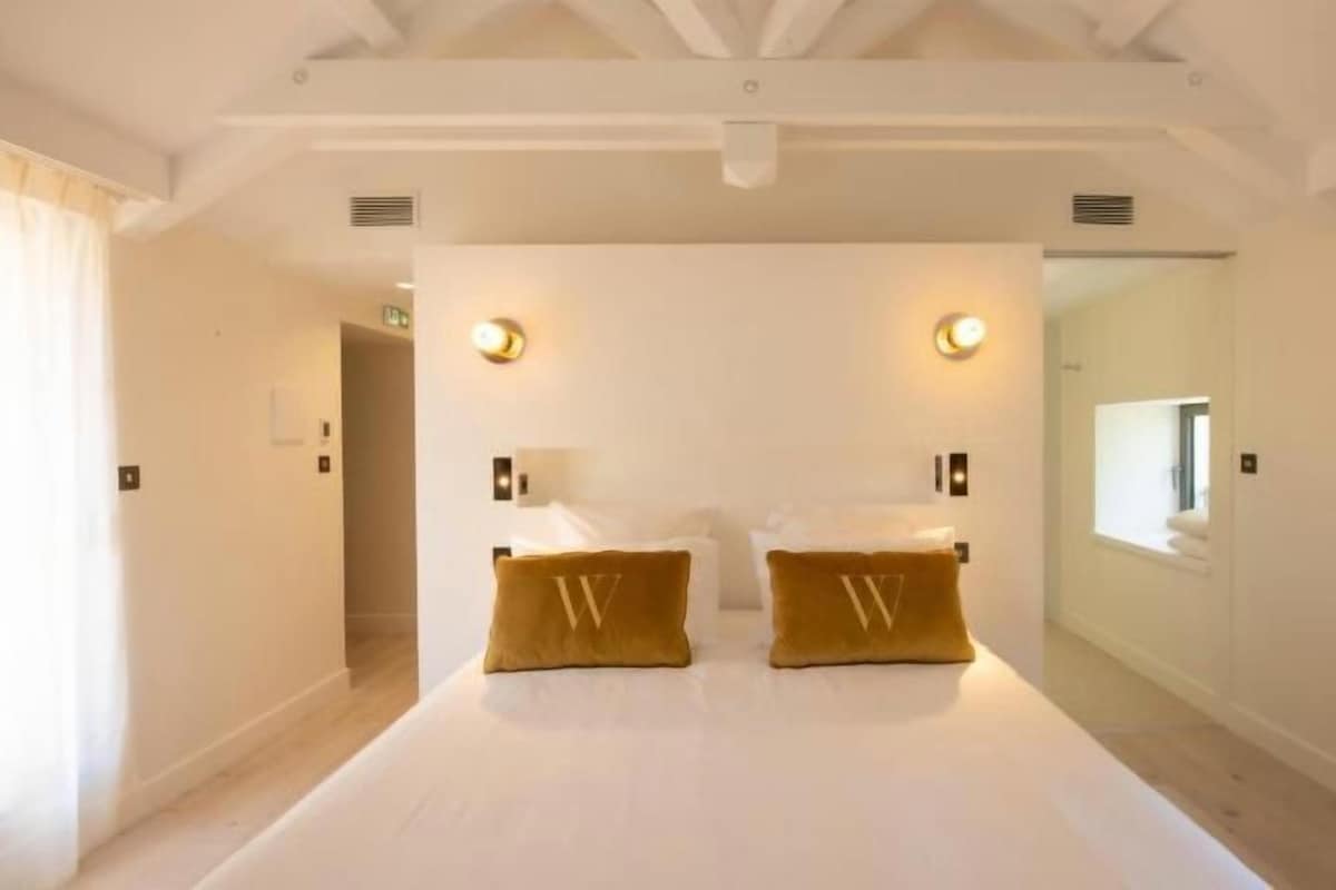 Een ruime slaapkamer met een groot bed, twee bedlampjes en een raam dat voor natuurlijk licht zorgt.