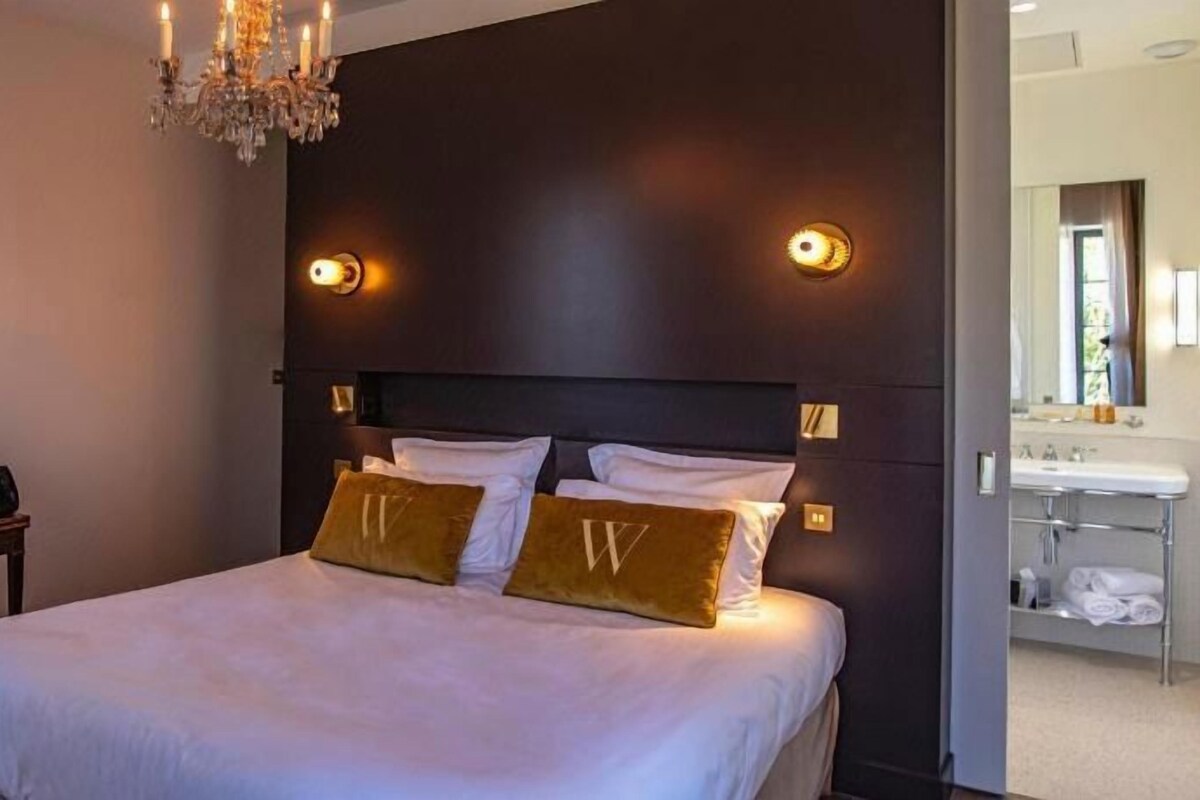 Een hotelkamer met een groot bed, nachtlampjes, een bureau en een stoel.