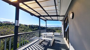A balcony with a wooden deck, white benches, and a metal railing.