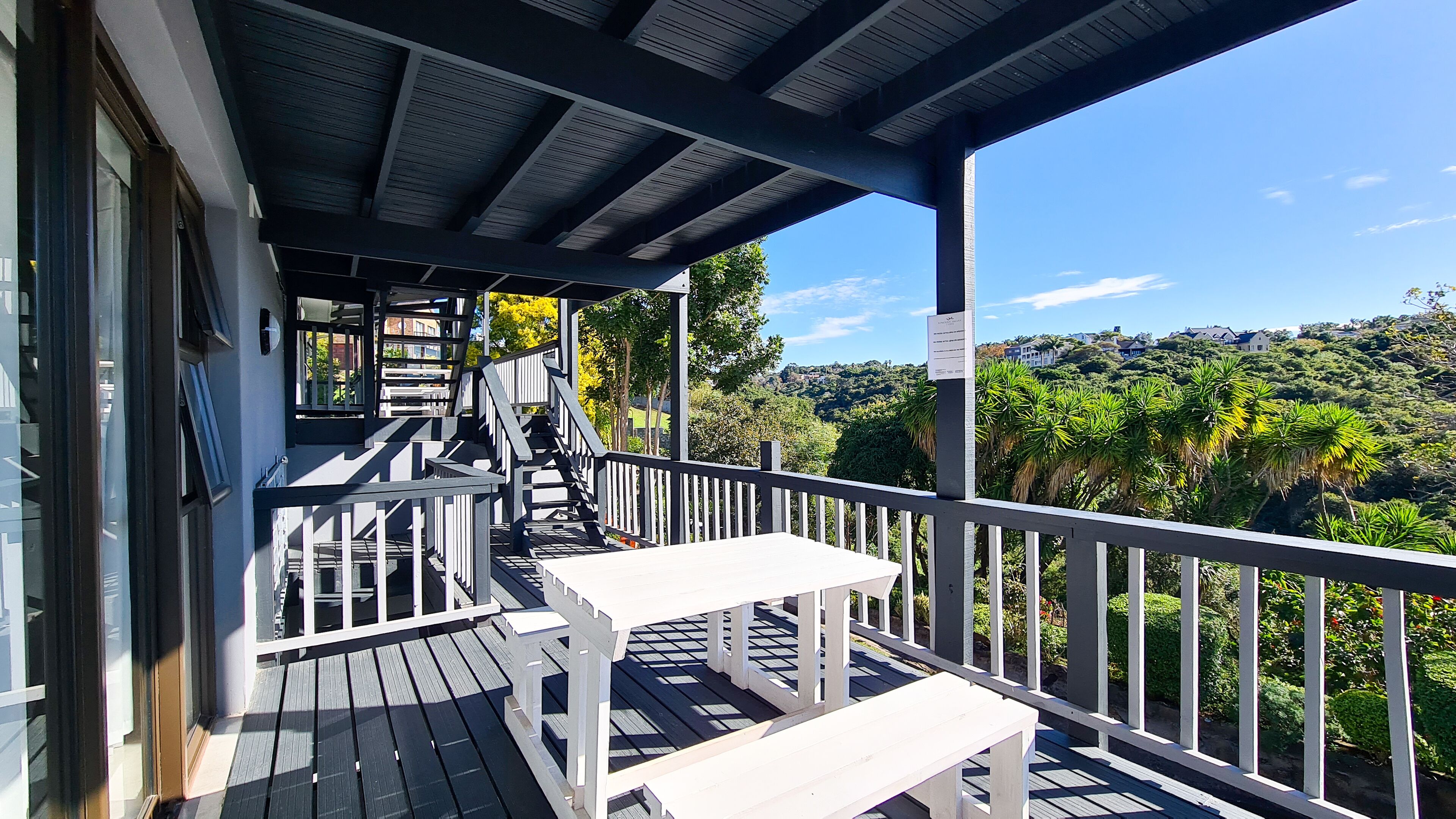 A wooden deck with a railing, a bench, and a staircase leading to an upper level.