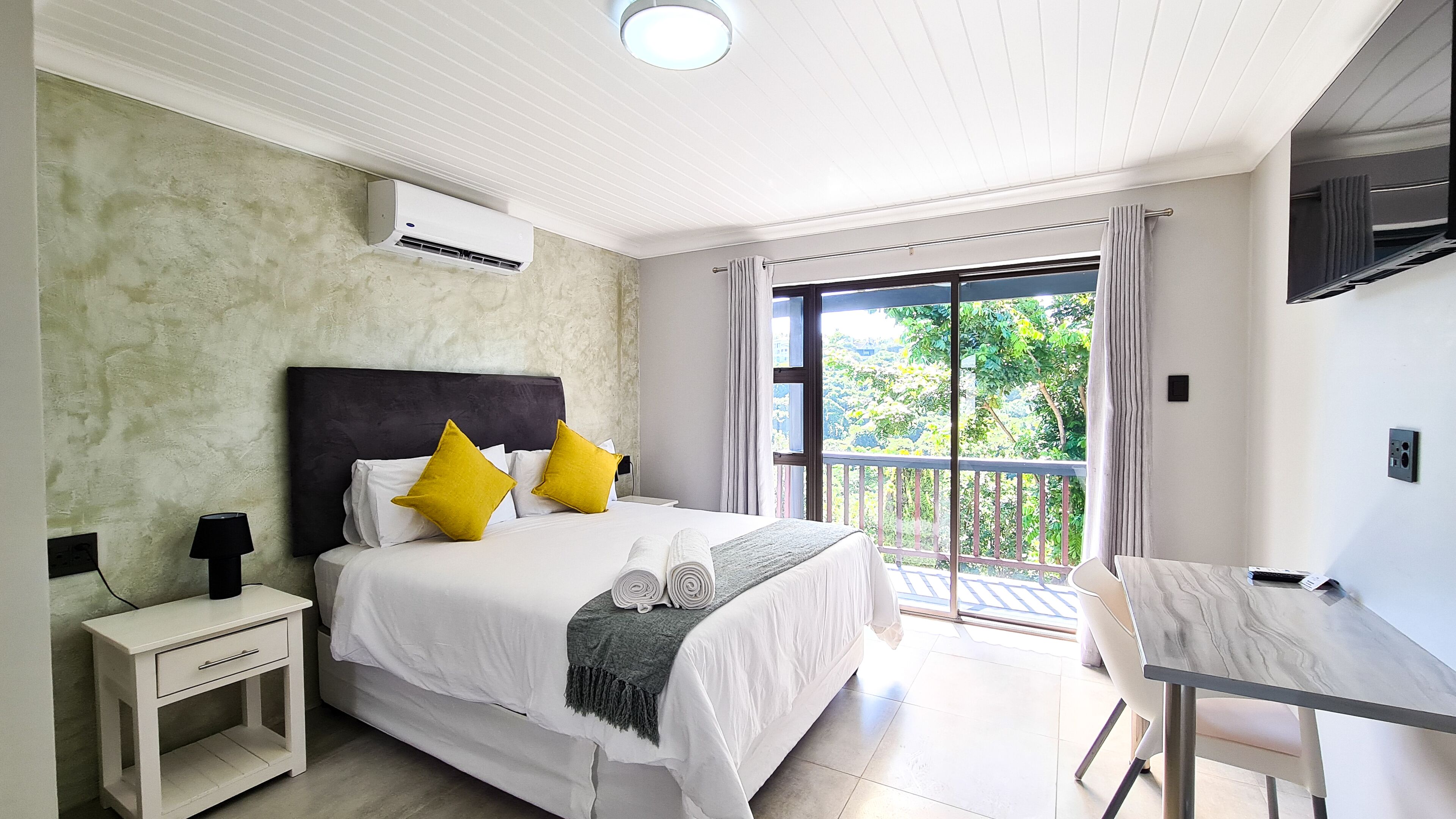 A hotel room with a bed, bedside table, and a desk with a chair.