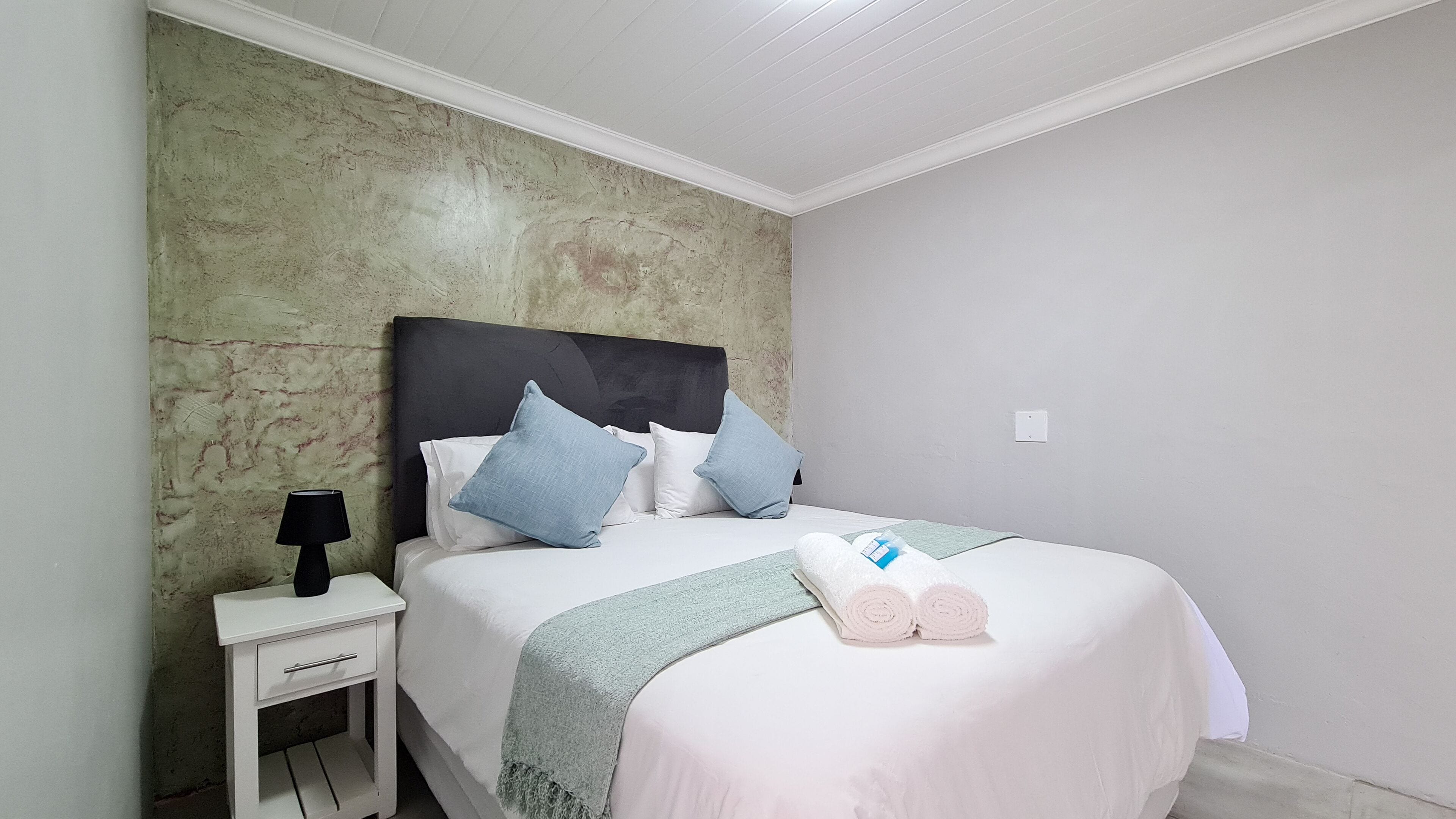 A neatly made bed with a white headboard, multiple pillows, and a rolled towel on the bed.