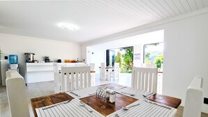 A bright, modern kitchen with white cabinetry, a wooden dining table set with white placemats, and a view of a lush garden through the open door. - Vincent Valley Lodge (East London)