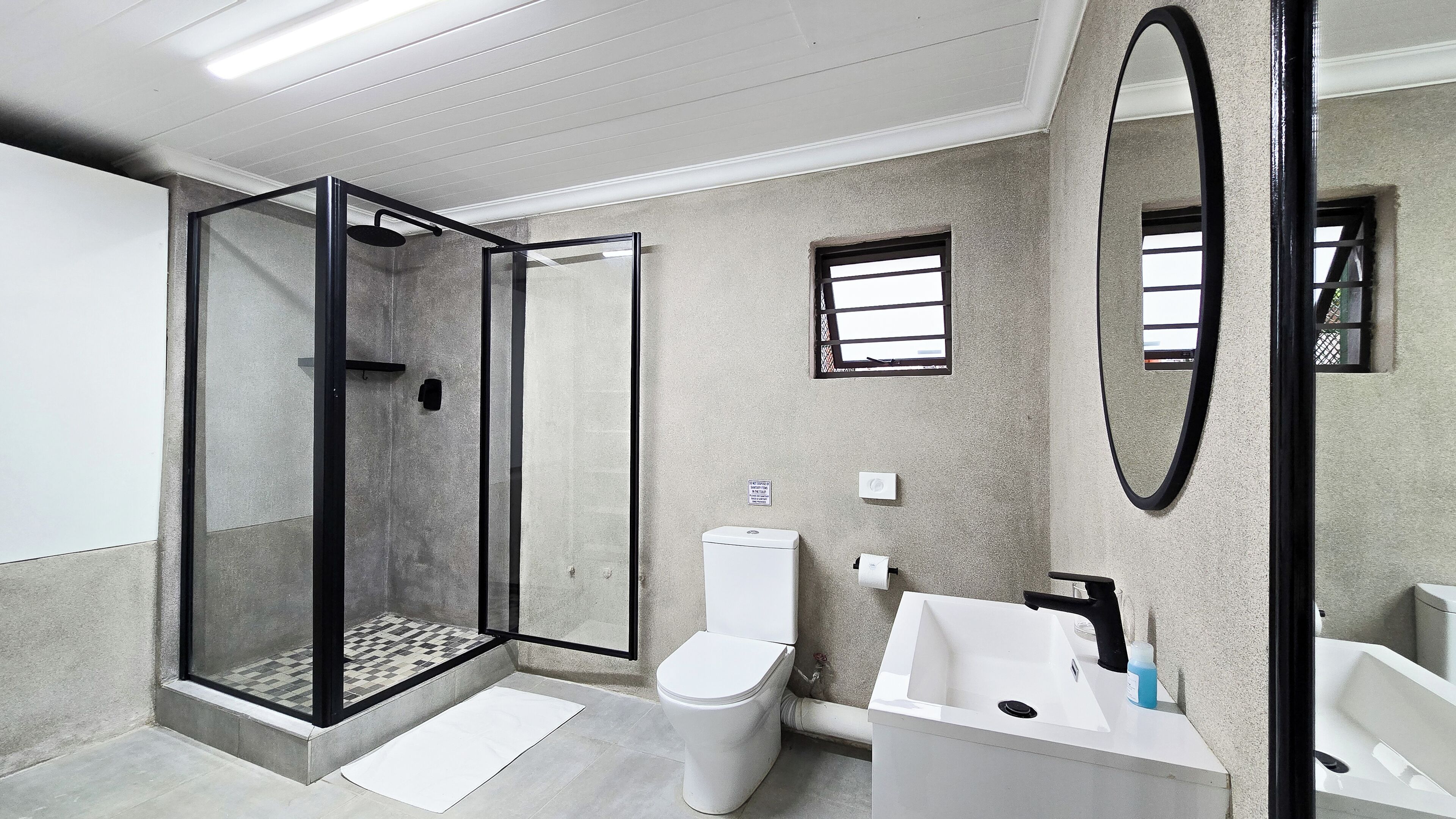 Un baño moderno con ducha de vidrio, inodoro, lavamanos y espejo.