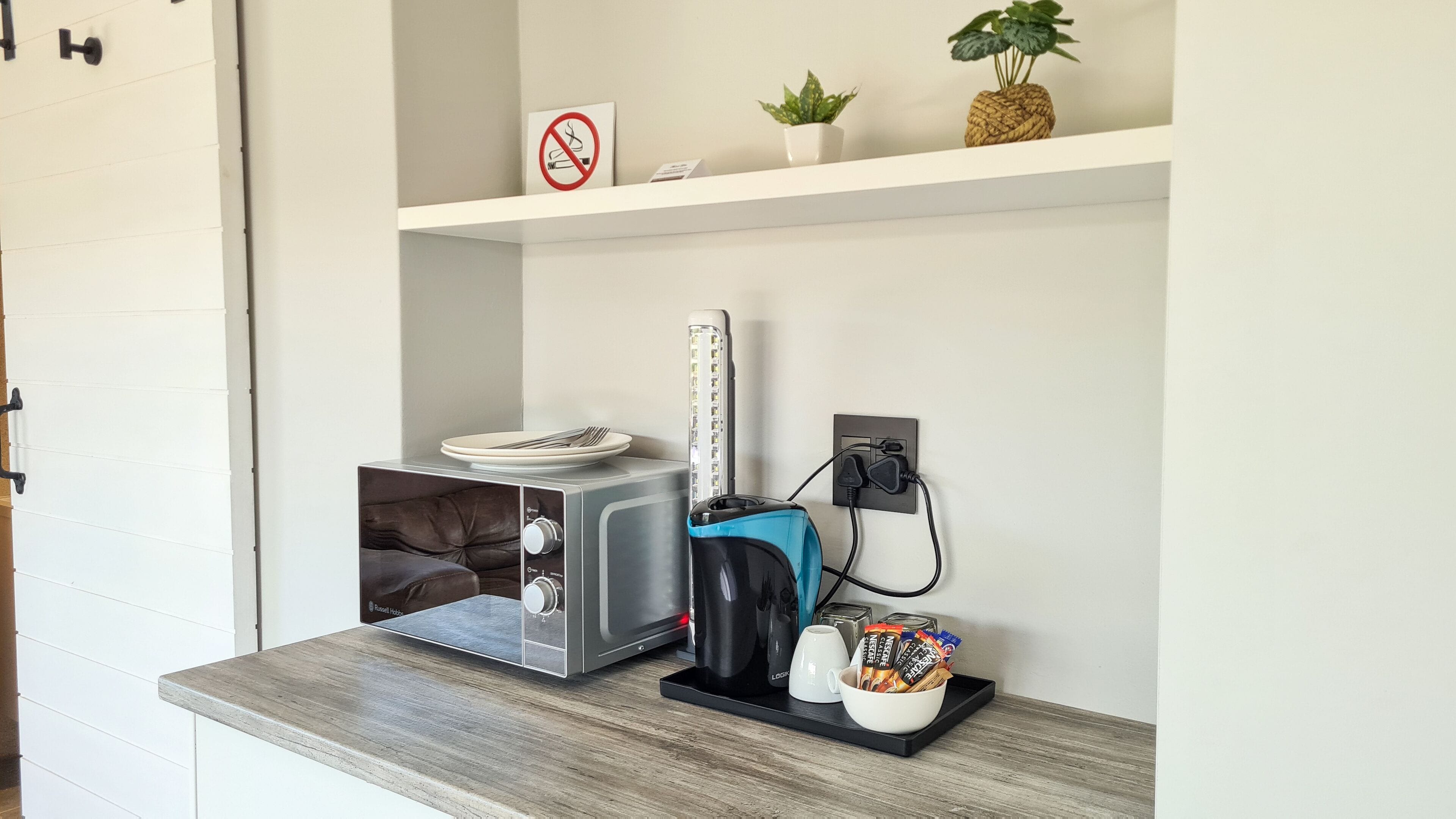 A kitchenette with a toaster, kettle, and a coffee maker on a wooden countertop.
