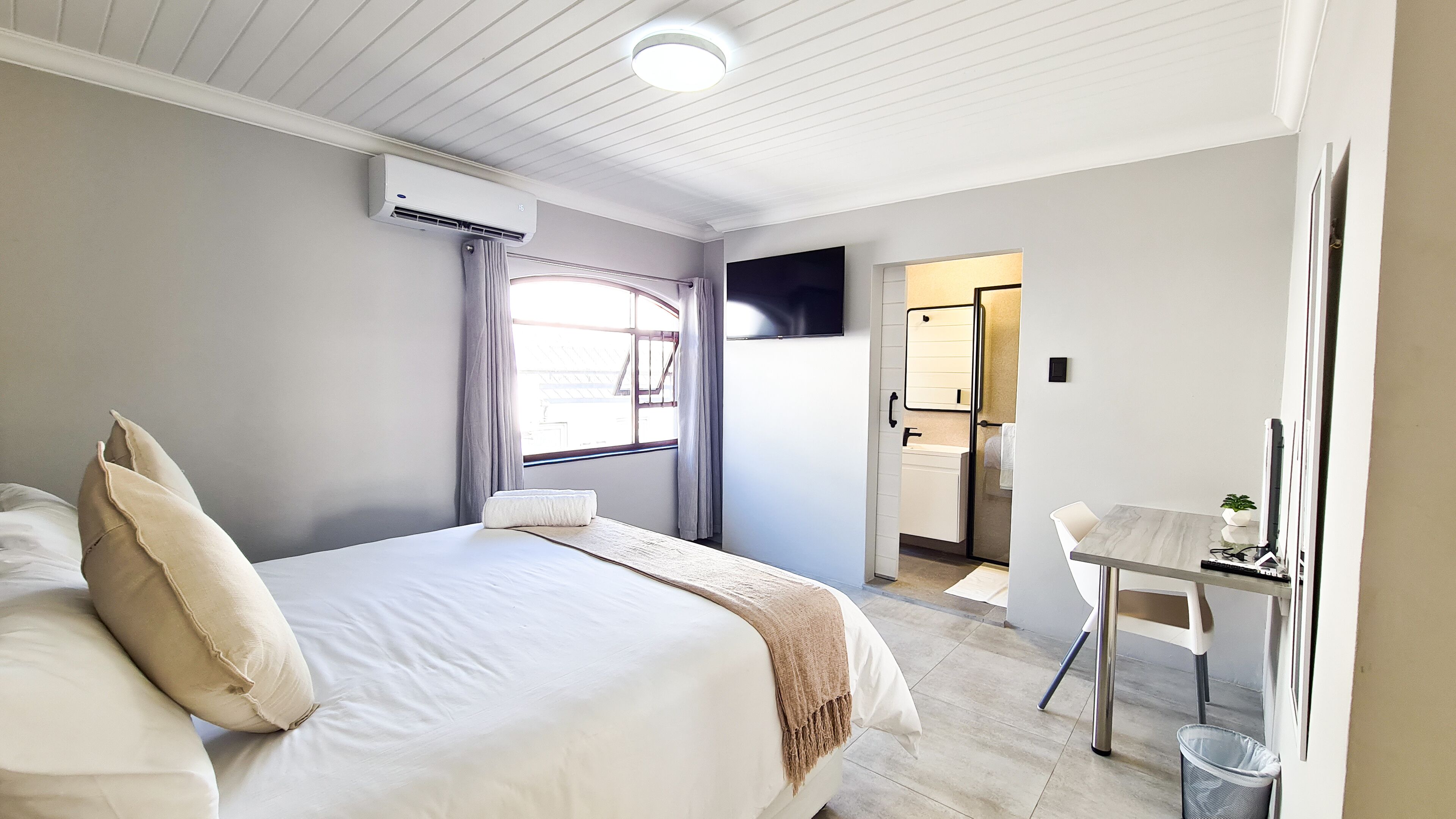 A bedroom with a bed, a desk, a chair, and a bathroom visible through an open door.