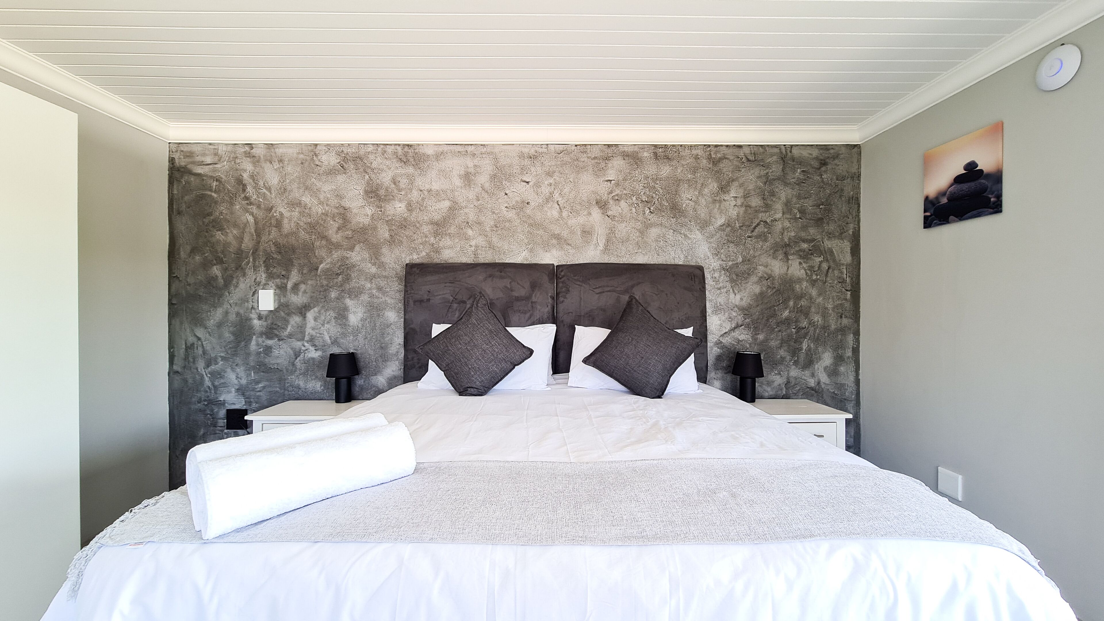 A bedroom with a large bed, two bedside tables, and a textured wall.