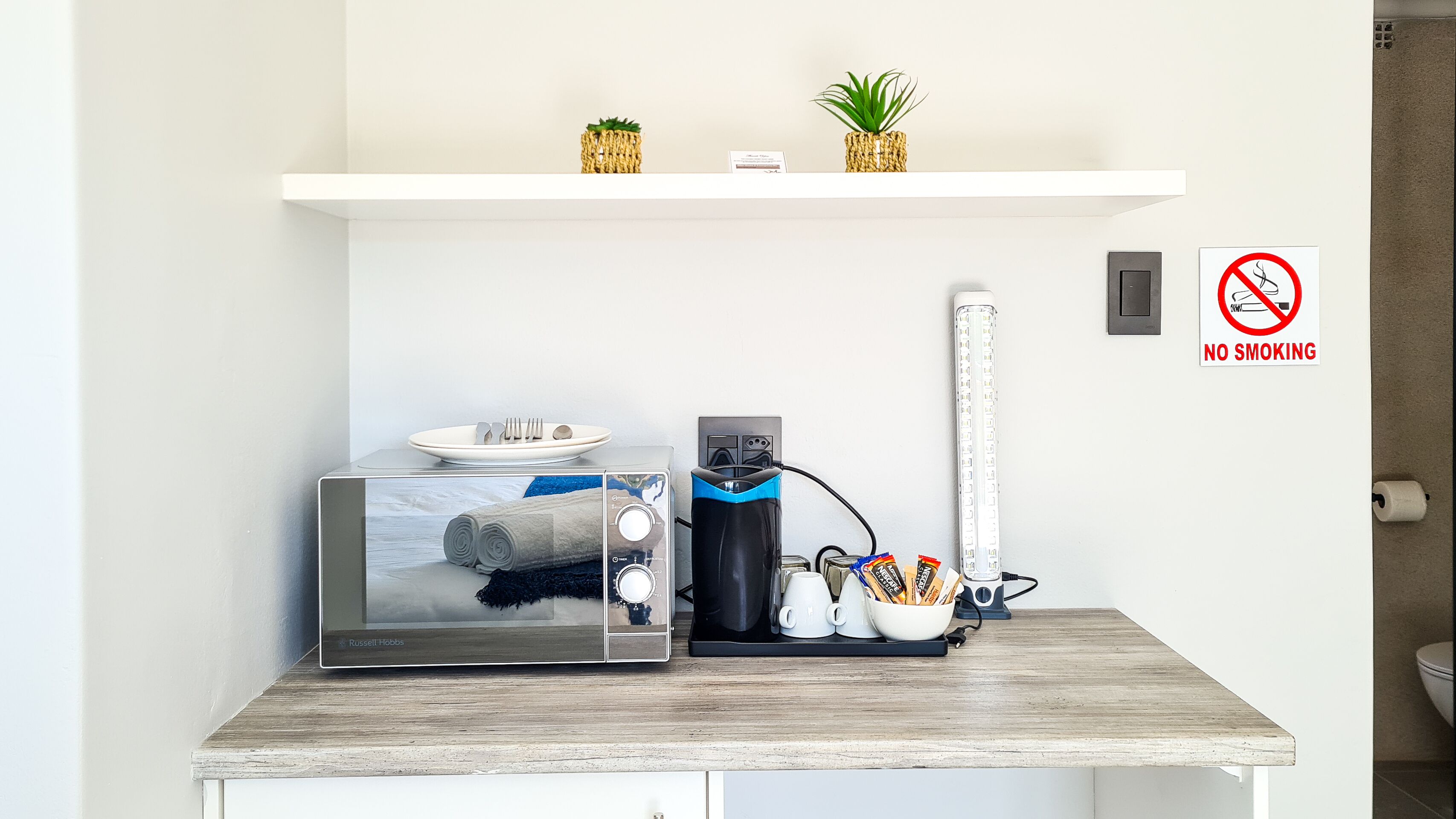Una kitchenette equipada con microondas, tostadora y cafetera. Hay un cartel de 'No Fumar' en la pared.